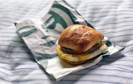 A Starbucks Impossible breakfast sandwich sitting on its bag on a striped cushion.