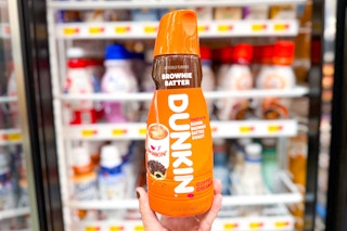 hand holding an orange bottle of Dunkin' Brownie Batter Creamer in front of the creamer area in the refrigerated aisle