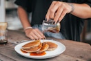 someone pouring maple syrup on pancakes