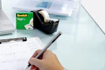 a tape dispenser on a desk with a person writing on a calendar