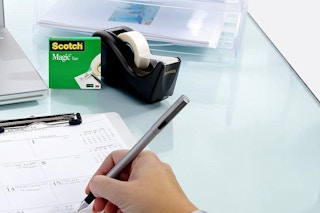 a person writing near a scotch tape dispenser