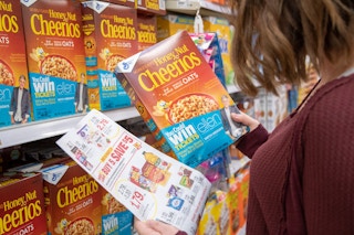 Person holding a a enwspapaer with sale items iin one hand and Cheerios in the other hand