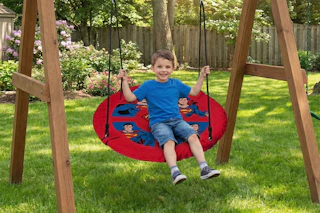 Lifestyle image of a Superman saucer swing being used outdoors by small child