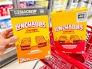 hand holding one package of Lunchables grilled cheesies next to another package in a red Target cart