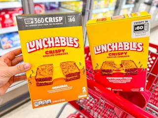 hand holding one package of Lunchables grilled cheesies next to another package in a red Target cart