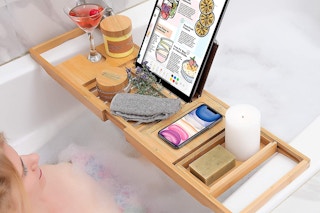 A woman sitting in a bath with a bamboo bathtub tray.