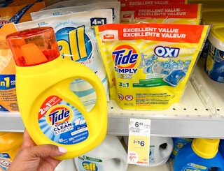 hand holding one bottle of Tide Simply liquid laundry detergent next to Tide Pods on shelf with sales tag underneath
