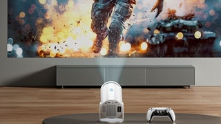 a projector next to a game controller on a table in front of a screen 