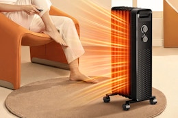Lifestyle image of the black Cowsar Space Heater being used indoors near someone sitting in a chair