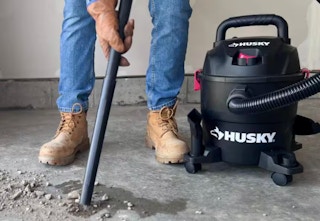 someone vacuuming up cement with the black Huskey wet/dry vacuum