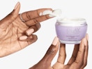 a hand holding a purple jar of face cream