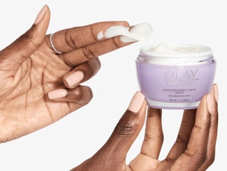 a hand holding a purple jar of face cream