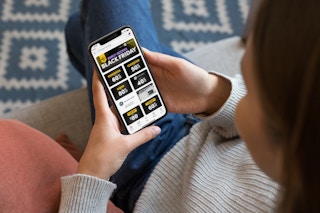 A woman looking at her phone displaying the Wayfair Black Friday deals page on their website.