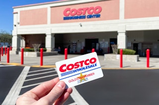 Someone holding up their Costco membership card in front of a Costco Business Center