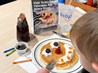a child eating a ihop scary face pancakes signage in restaurant