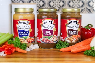 three jars of heinz gravy on a kitchen counter next to vegetables 