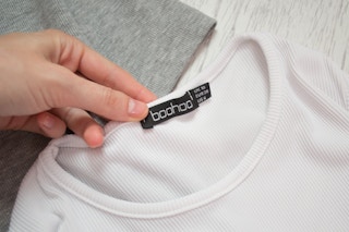 A hand holding the tag of a Boohoo shirt
