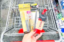 person holding loreal mascara, eyeliner, foundation, and lipstick over a cart