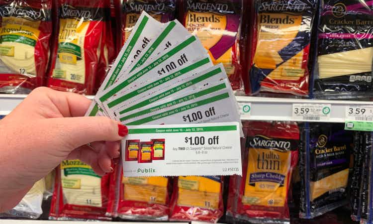 Hand holding eight paper Publix coupons for Sargento cheese in front of Sargento cheese selection
