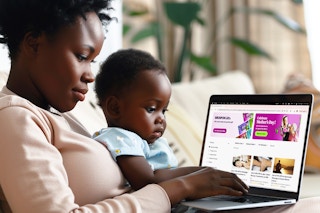 a mom with a baby on her lap looking at a laptop with groupons mother's day deals on screen