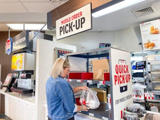 A woman standing at the pickup counter inside a KFC restaurant.