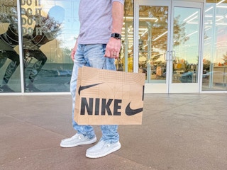 A person standing outside of a Nike store, holding a Nike shopping bag