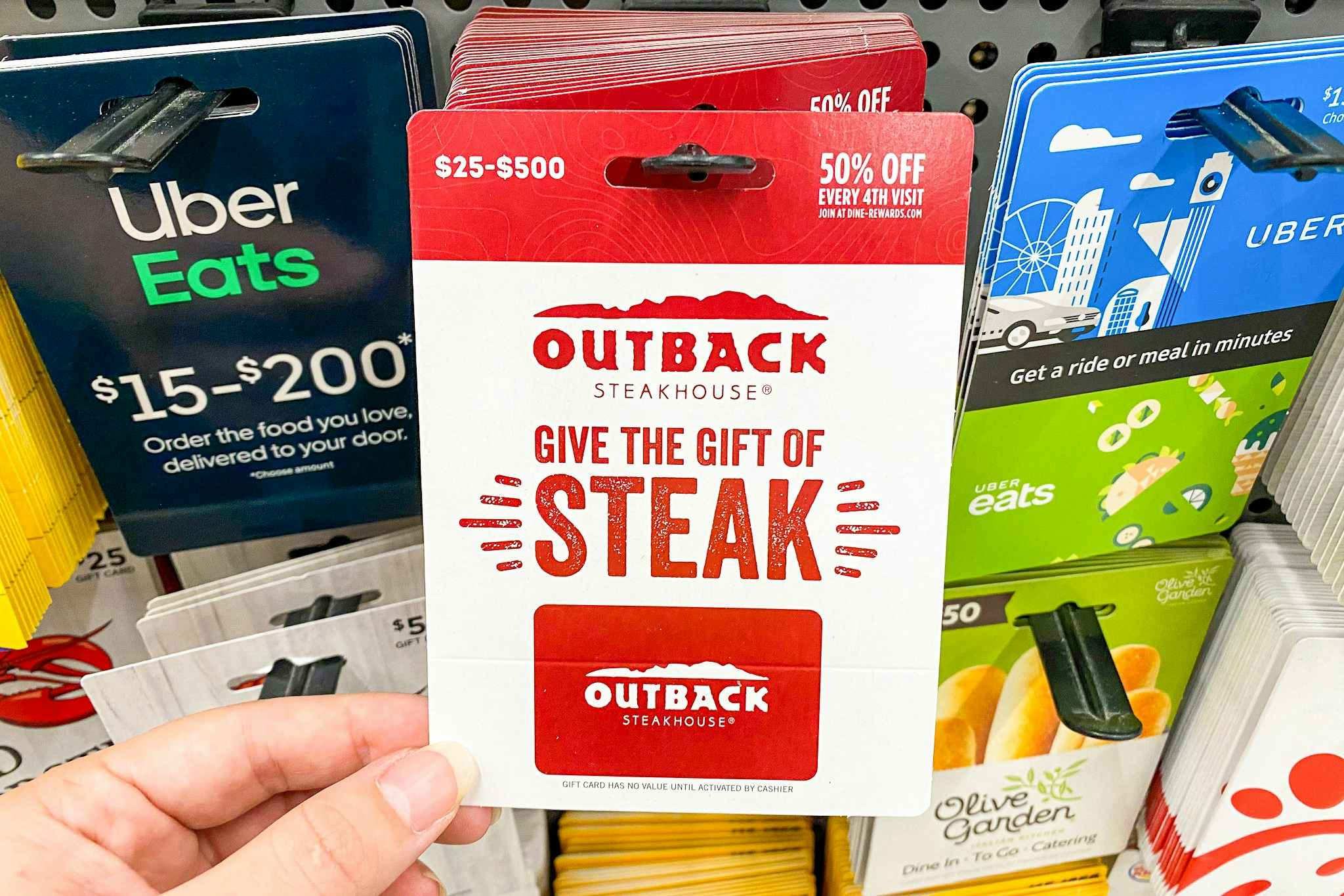 A person's hand taking an Outback Steakhouse gift card from a display of gift cards at Walmart.