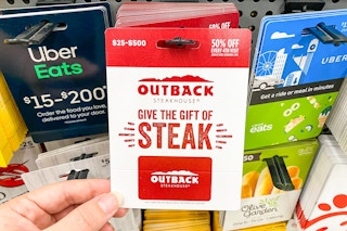 A person's hand taking an Outback Steakhouse gift card from a display of gift cards at Walmart.