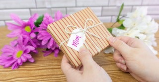 Someone holding a gift with a tag that says "Mom" over a table with flowers