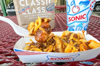 a person about to eat sonic chili tots and a drink outside sonic