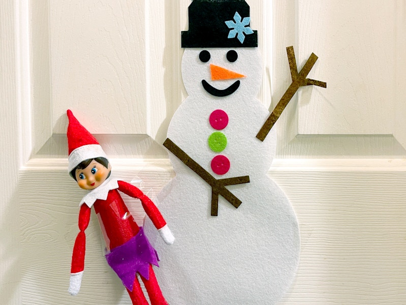 elf on the shelf hanging near decorated snowman on door