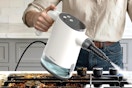 Woman using the TEEVOGO Handheld Steam Cleaner on her oven.