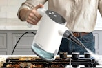 Woman using the TEEVOGO Handheld Steam Cleaner on her oven.