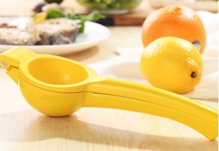 Yellow lemon squeezer on a table with food and a lemon