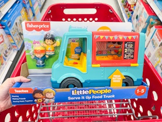 A little People Food Truck toy held out by hand in front of a shopping cart.