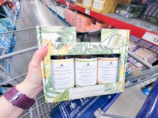 hand holding a 3-pack of essenza hand soap in glass bottles in a cart