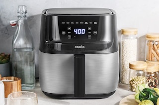 A Cook's 6-Quart Digital Air Fryer on a counter top with a bottle of water to one side and spices on the other