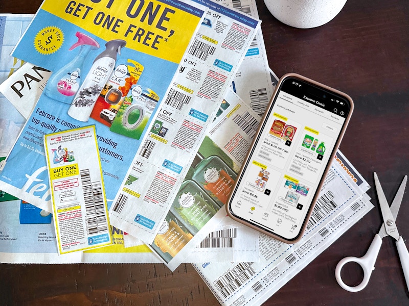 A phone displaying digital coupons in the Dollar General app on a table with some paper manufacturer coupons that have been cut