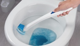 a hand cleaning a toilet with a toilet scrubber 
