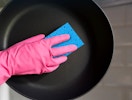 a hand cleaning a skillet with a blue sponge