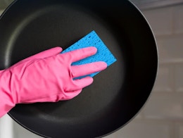 a hand cleaning a skillet with a blue sponge