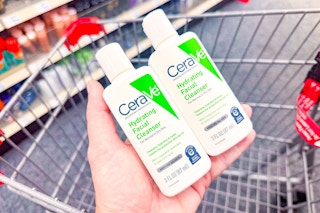 person holding 2 cerave cleansers over a cart