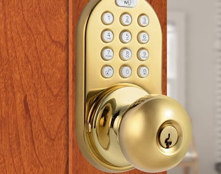 A polished brass keypad doorknob on a door.
