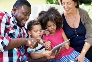 Parents looking at a tablet with their kids while the dad points at something on the screen.