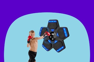 A boy in boxing gloves punches a 5-petal flower shaped music boxing machine, which is black with blue lights and on the wall.