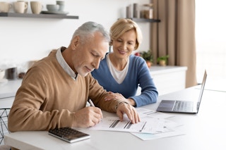 A couple sitting at a table, working on financial paperwork together.