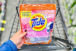 person holding a bag of tide xl pods over a cart