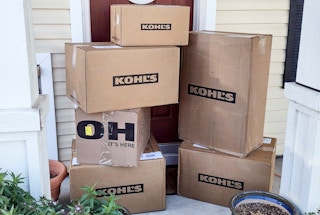 A stack of Kohl's delivery boxes sitting on a front porch.