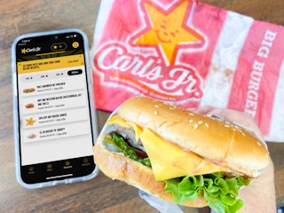 a person holding a cellphone with the carls jr app being held next to a carls jr burger