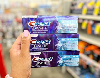 three tubes of Crest toothpaste in hand